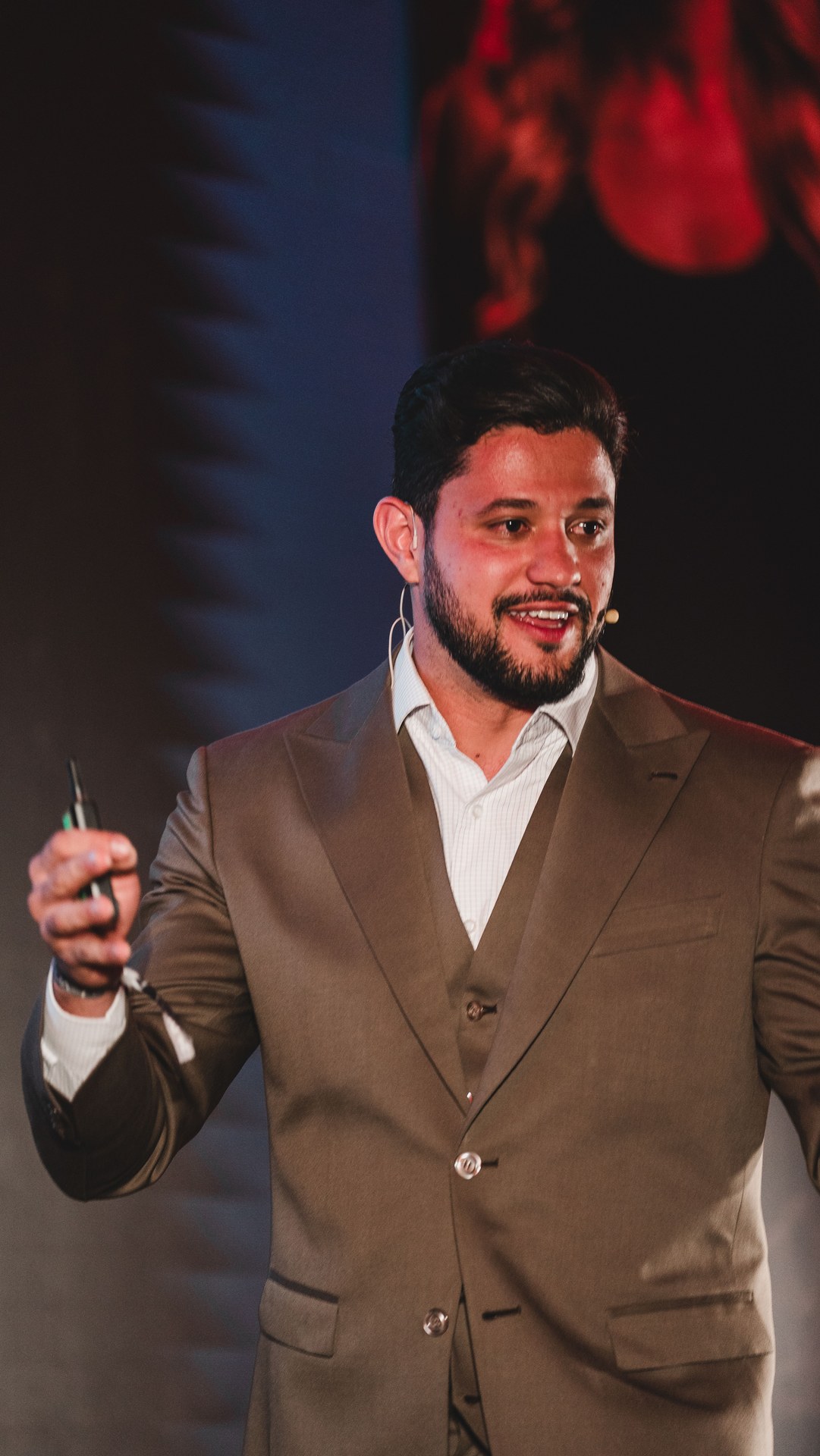 Vitor Rehbein de terno claro falando no palco com microfone de lapela