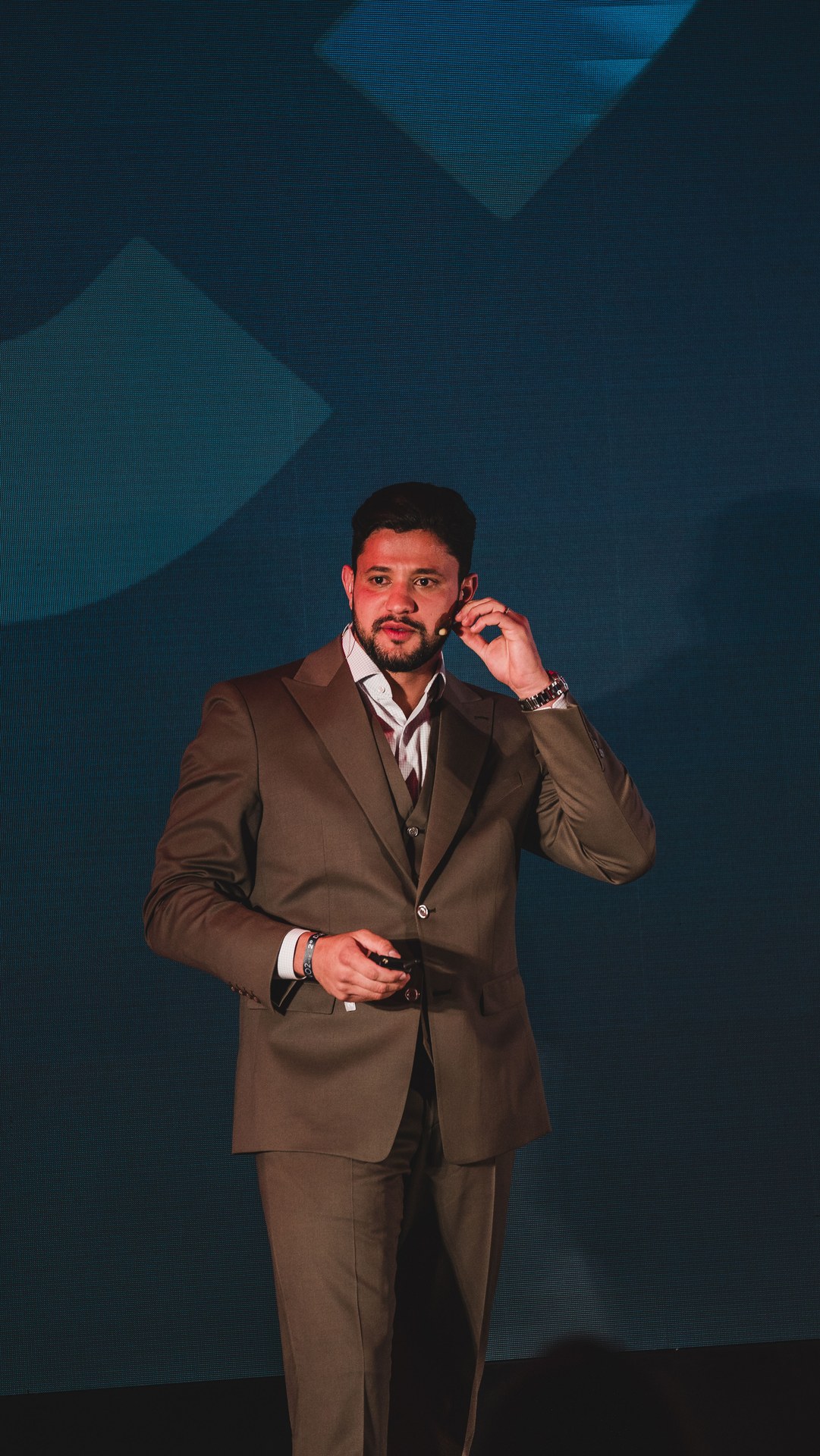 Vitor Rehbein de terno claro no palco, fundo azul escuro